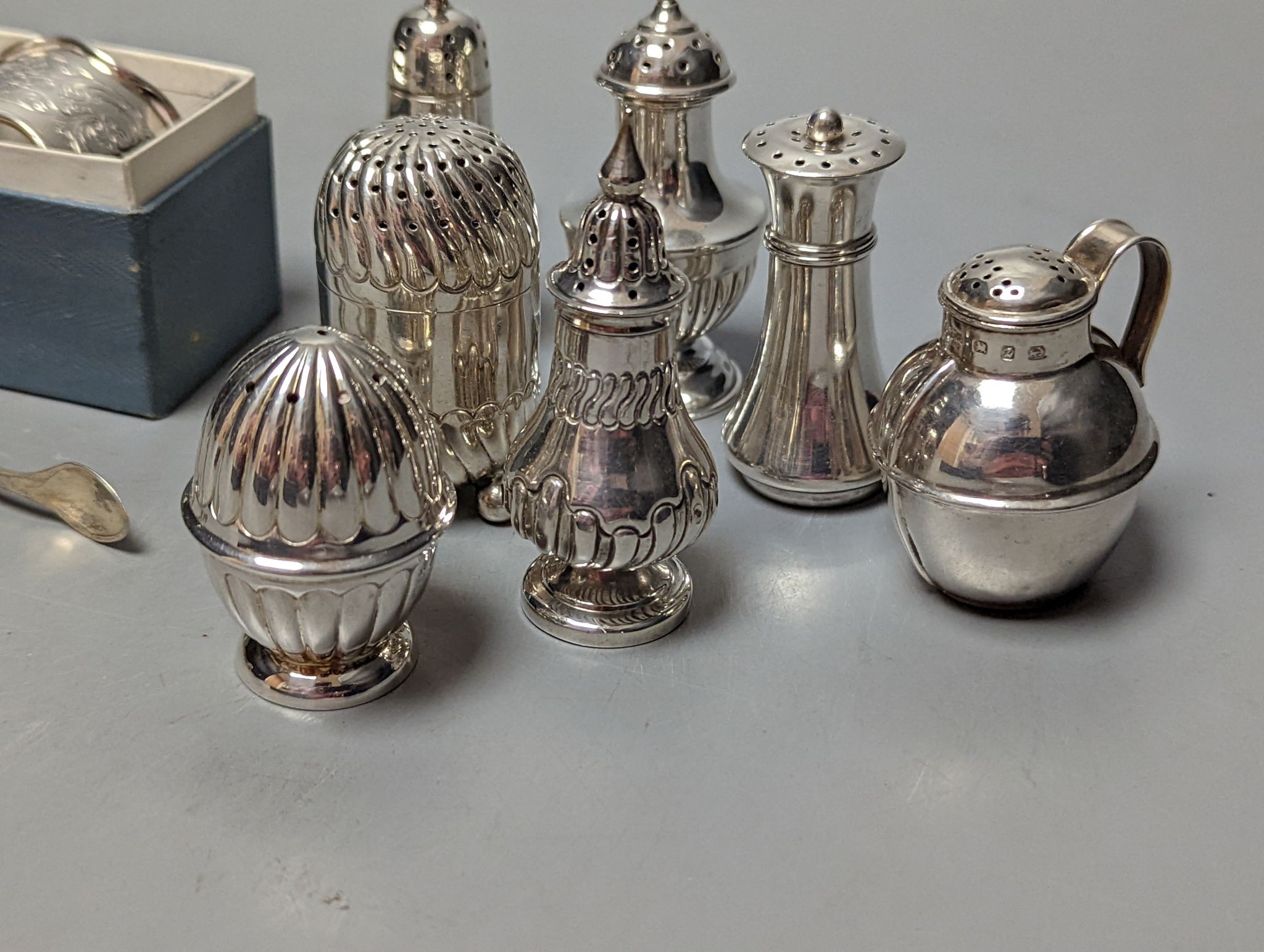 A cased silver napkin ring, seven assorted silver pepperettes including Guernsey can and a pair of plated sugar tongs.